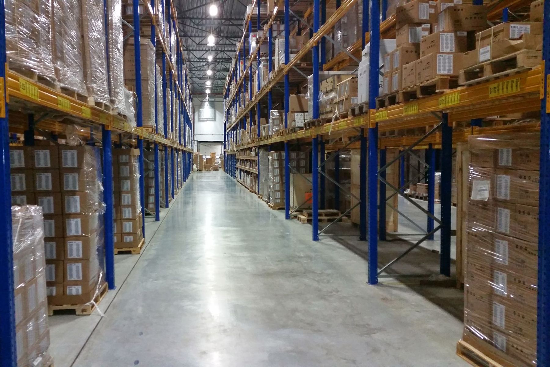 Long warehouse aisle lined with tall pallet racks stacked with boxed goods
