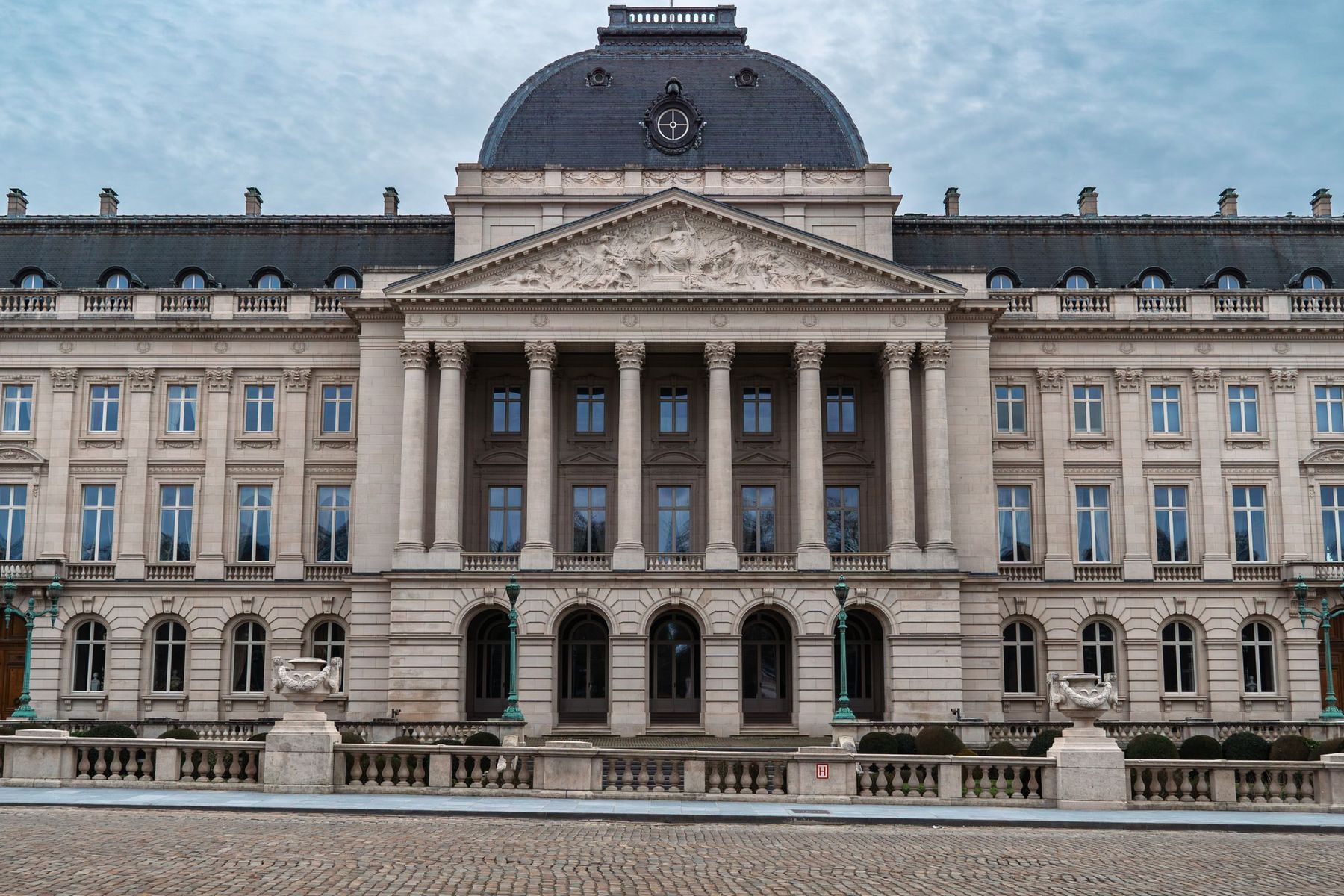 Symmetrical neoclassical façade with a columned central portico, pediment and dome under a cloudy sky