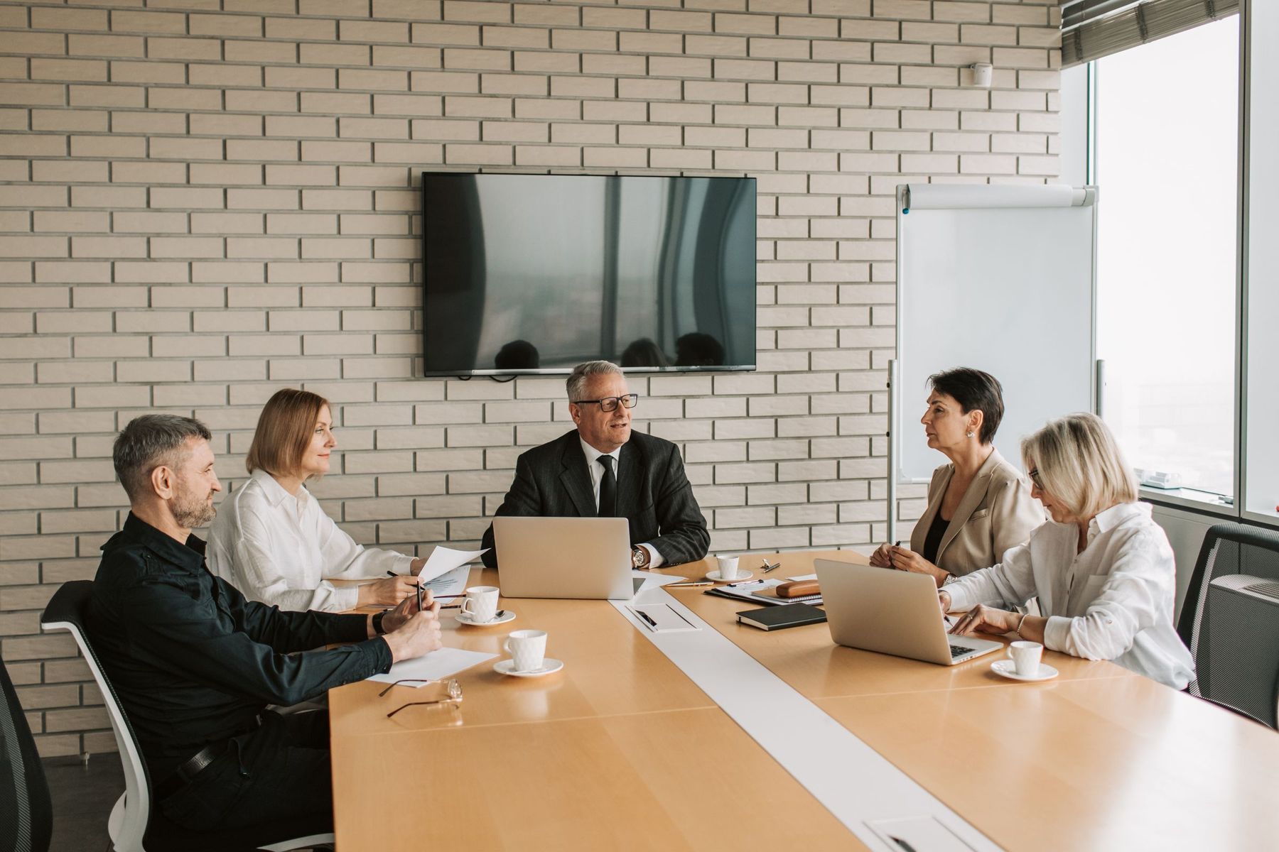 Five professionals meeting around a conference table with laptops and papers