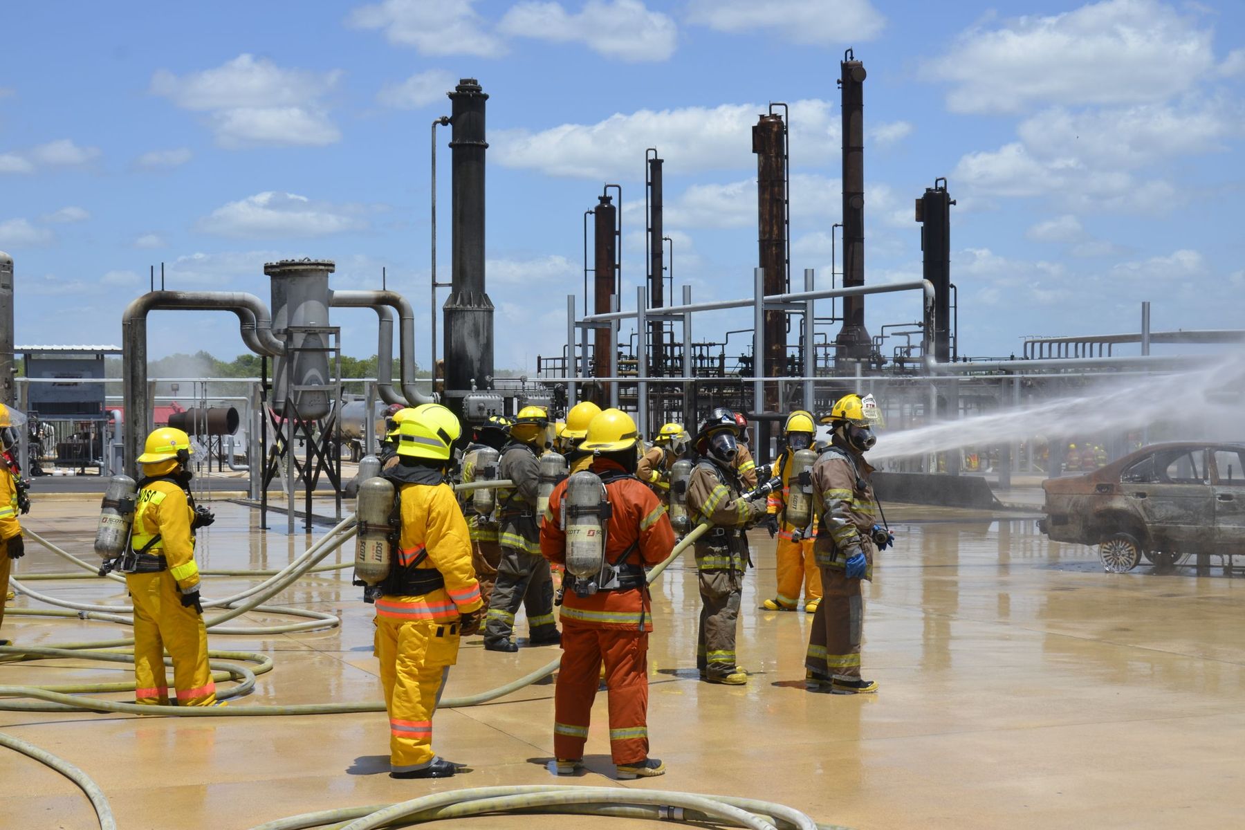 Firefighters in helmets and breathing apparatus spraying water during a training drill at an industrial plant